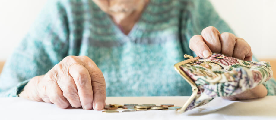 Elderly woman opens her coin purse over a table while counting the coins.