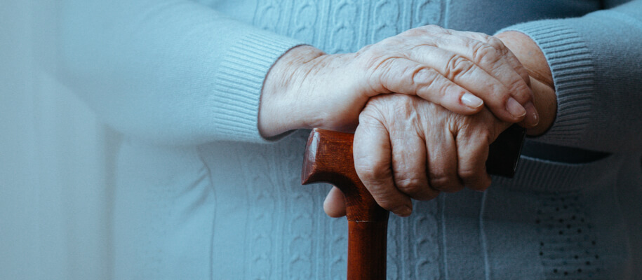 An elderly woman's hands are placed on top of her cane as she contemplate respite care options.