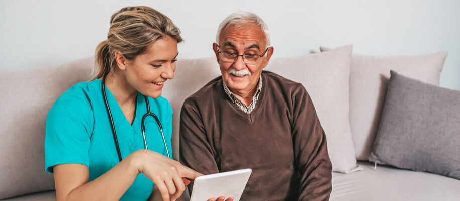 A nurse shows a senior man something on a tablet.