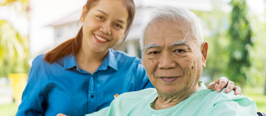 A woman caregiver smiling standing next to a senior resident.